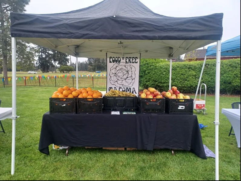 A market stand featuring fresh produce underneath a canopy with a Food is free Tacoma sign 